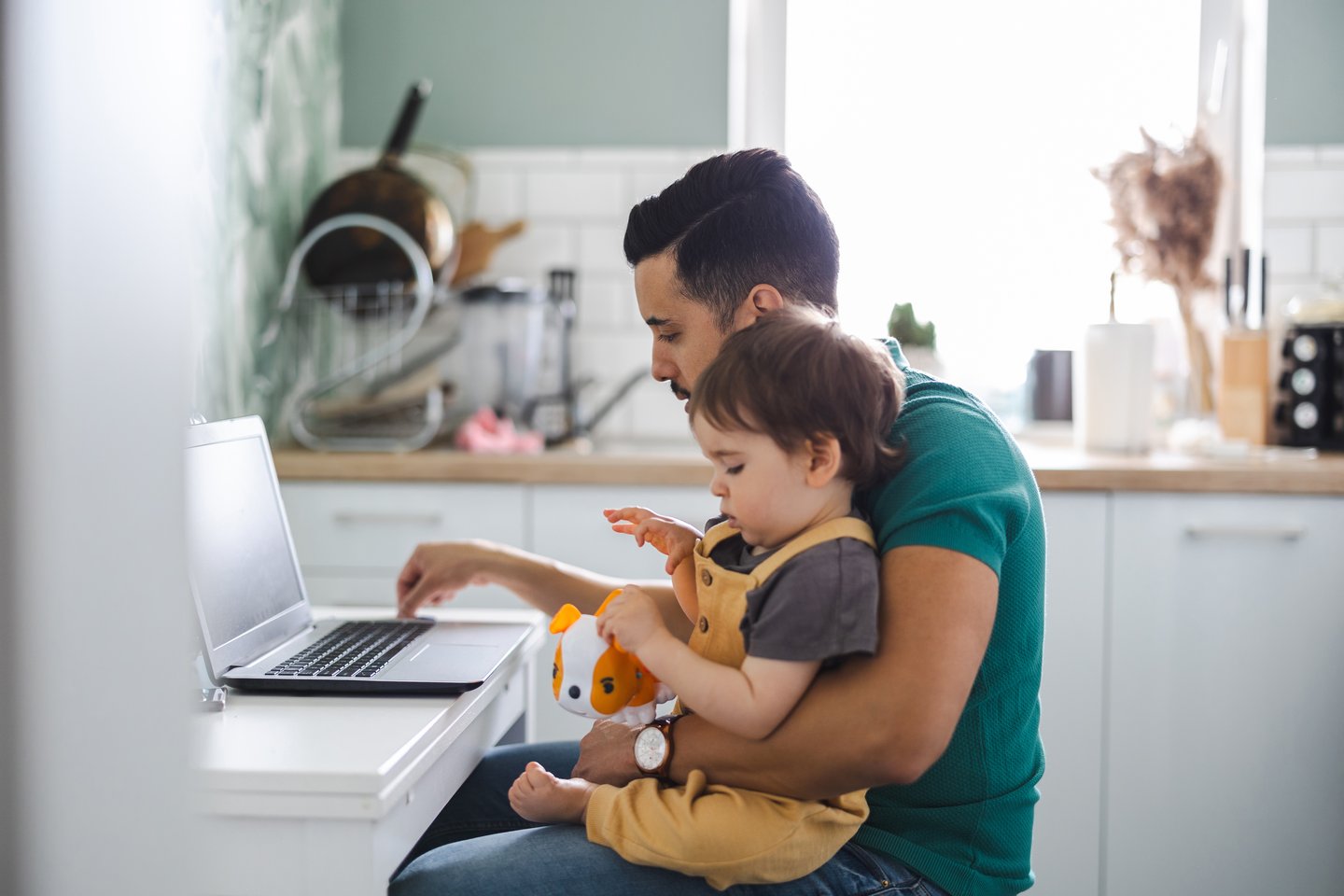 Picture of a dad looking at his laptop with his toddler son sitting on his lap