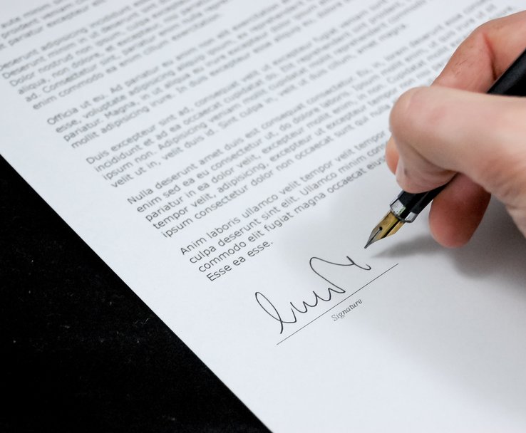 Hand holding a pen ready to sign a document.