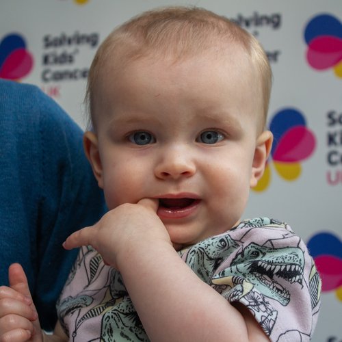 Picture of baby in front of a Solving Kids' Cancer UK branded banner