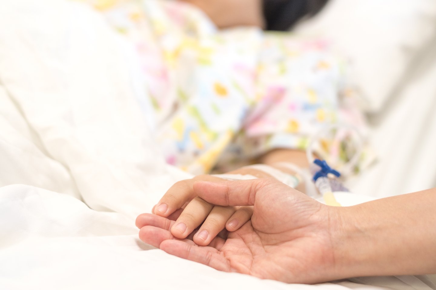 Parent holding a child's hand while they're laying in a hospital bed