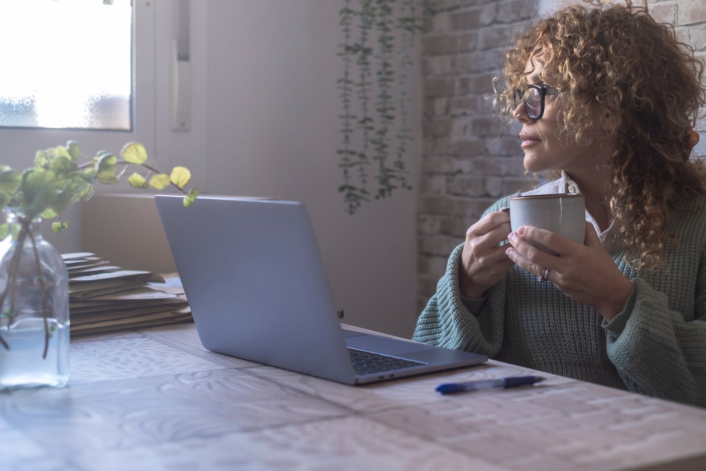 Woman sitting at a kitchen table holding a mug in front of a laptop