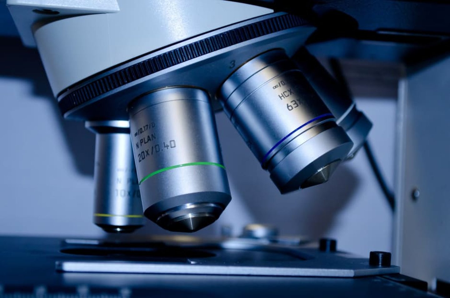Close-up of a grey microscope, four objective lenses and the microscope stage are visible.