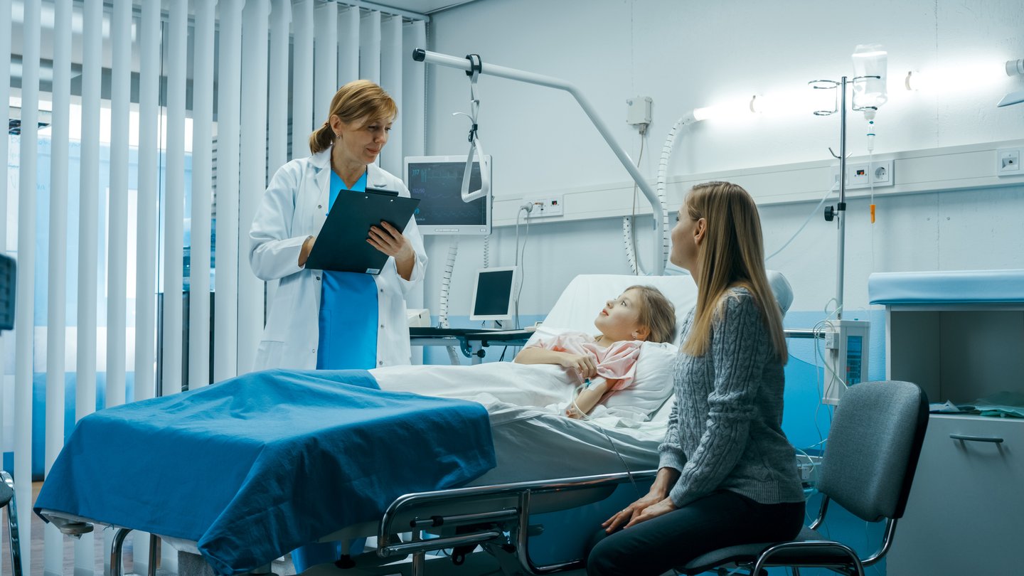 Girl in hospital bed talking to a doctor with her mother