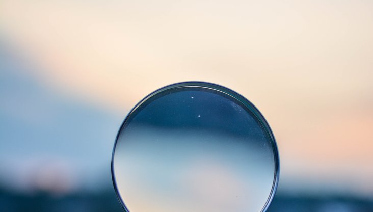 A hand holding-up a magnifying glass against an out of focus blue skyline.