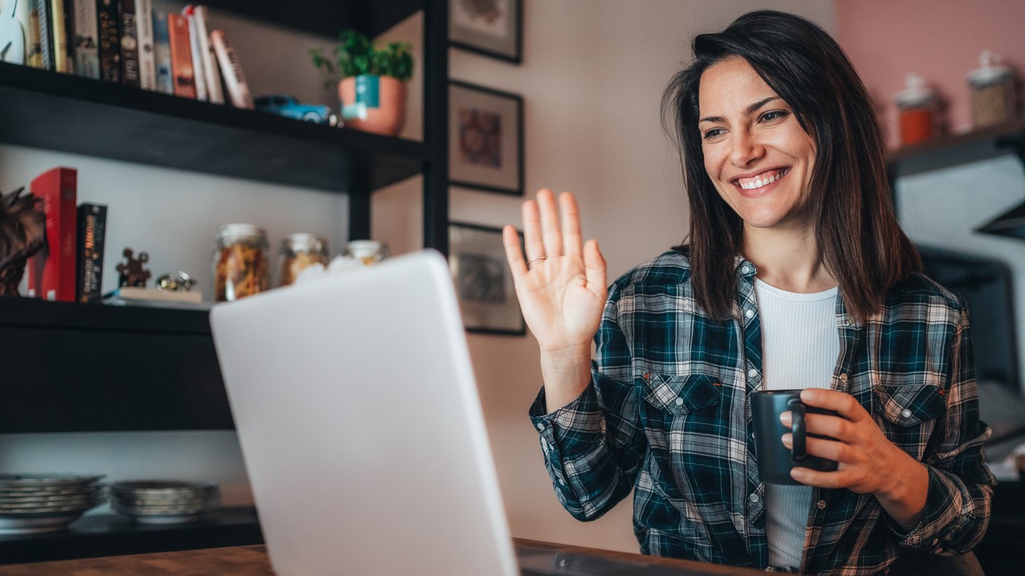 Woman holding a mug, smiling at a laptop while on a video call