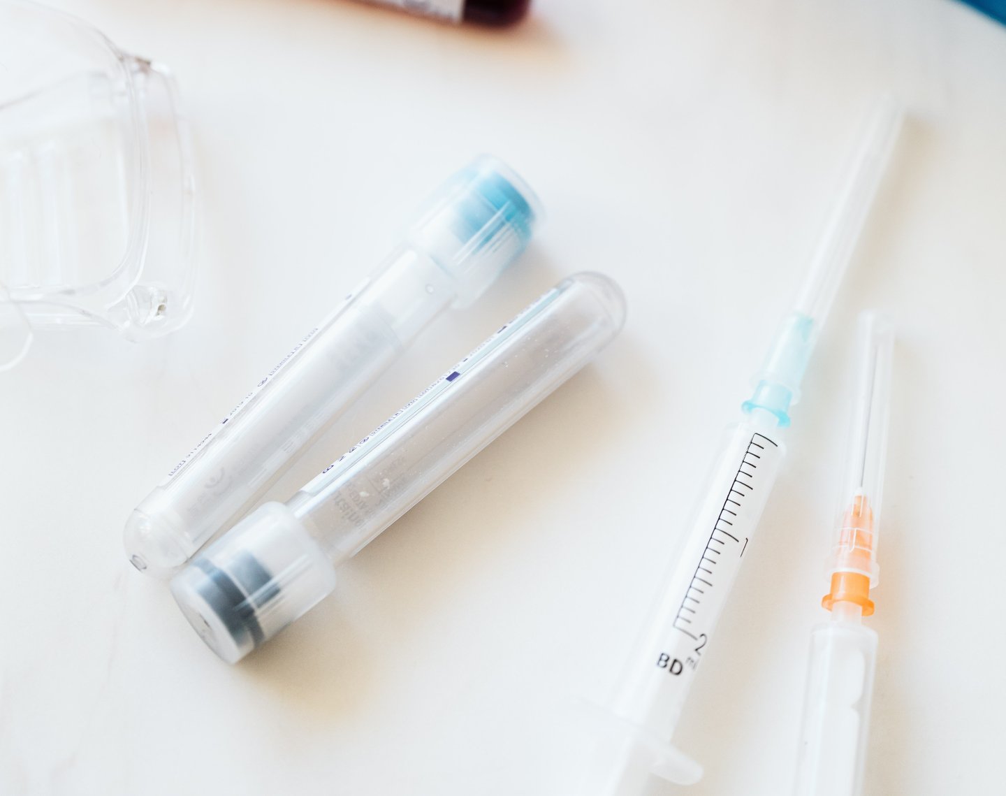 Two clear medical test tubes and a syringe on a white surface.