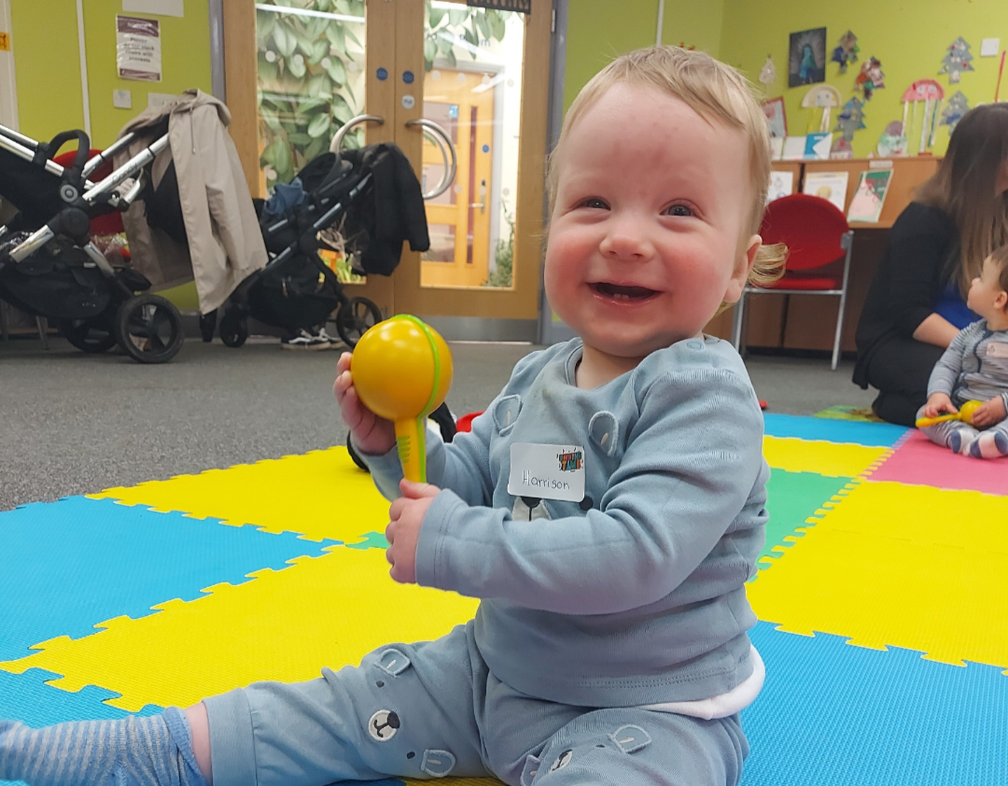 Picture of a child smiling while playing with a yellow maraca