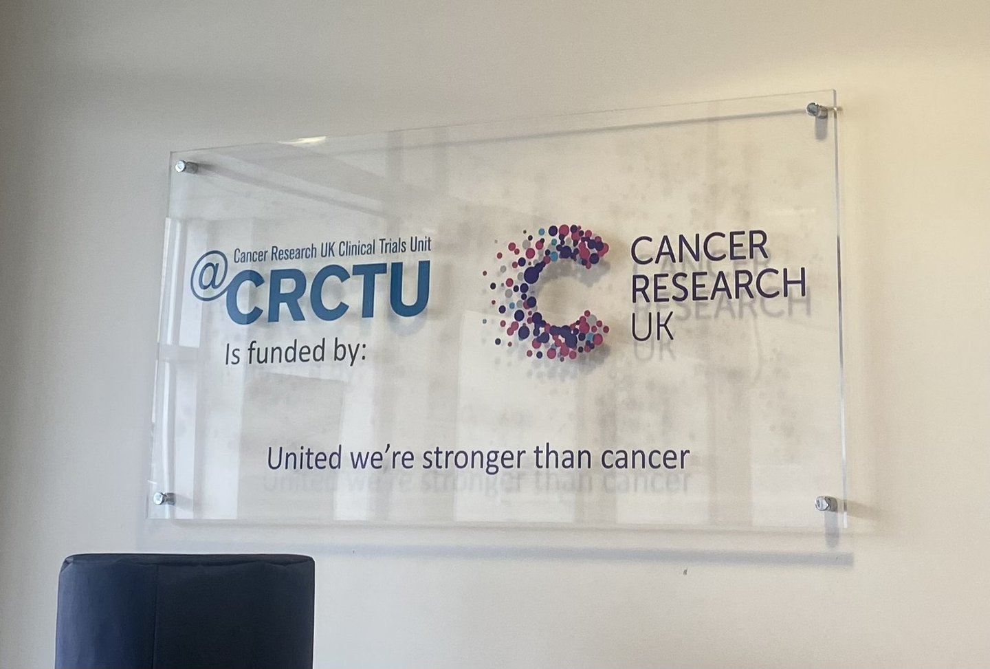 Glass sign. Left: ‘Cancer Research UK Clinical Unit Trial is funded by:’. Right Cancer Research logo. Bottom: ‘United we’re stronger than cancer’.