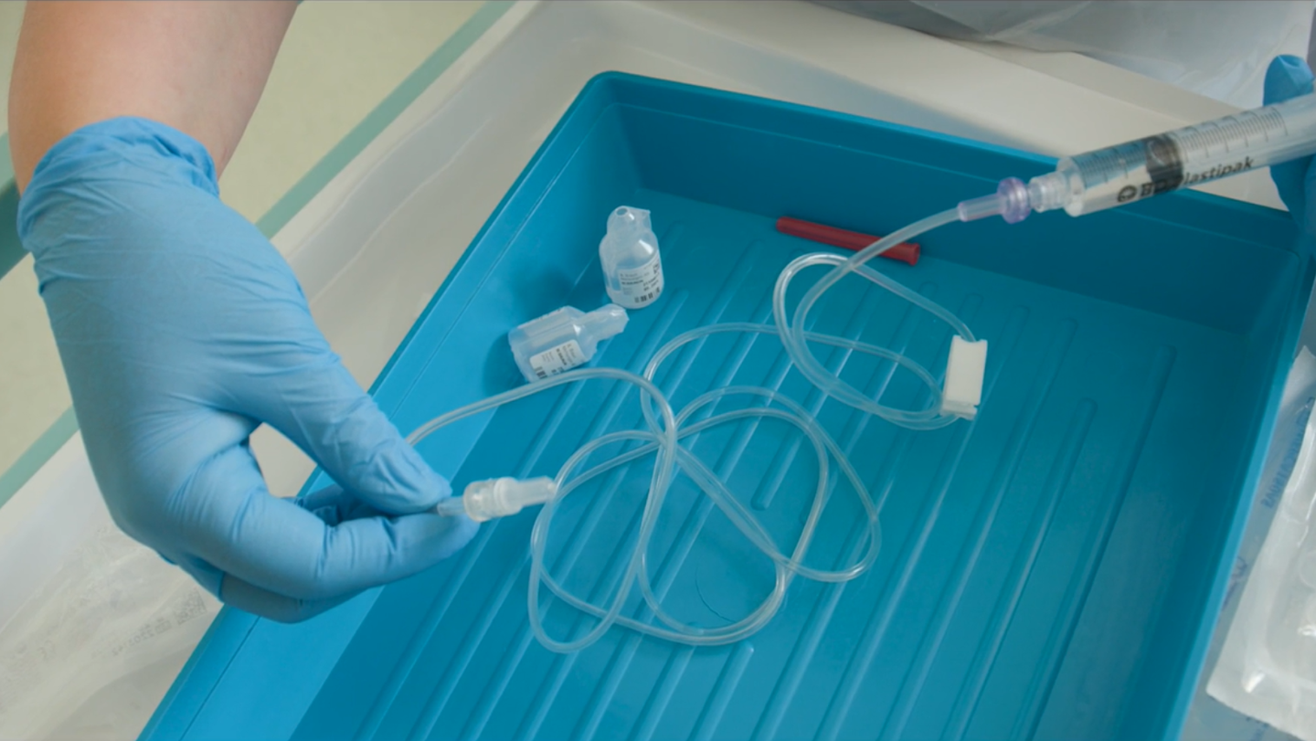 Gloved hand handling a medical syringe with tubing attached