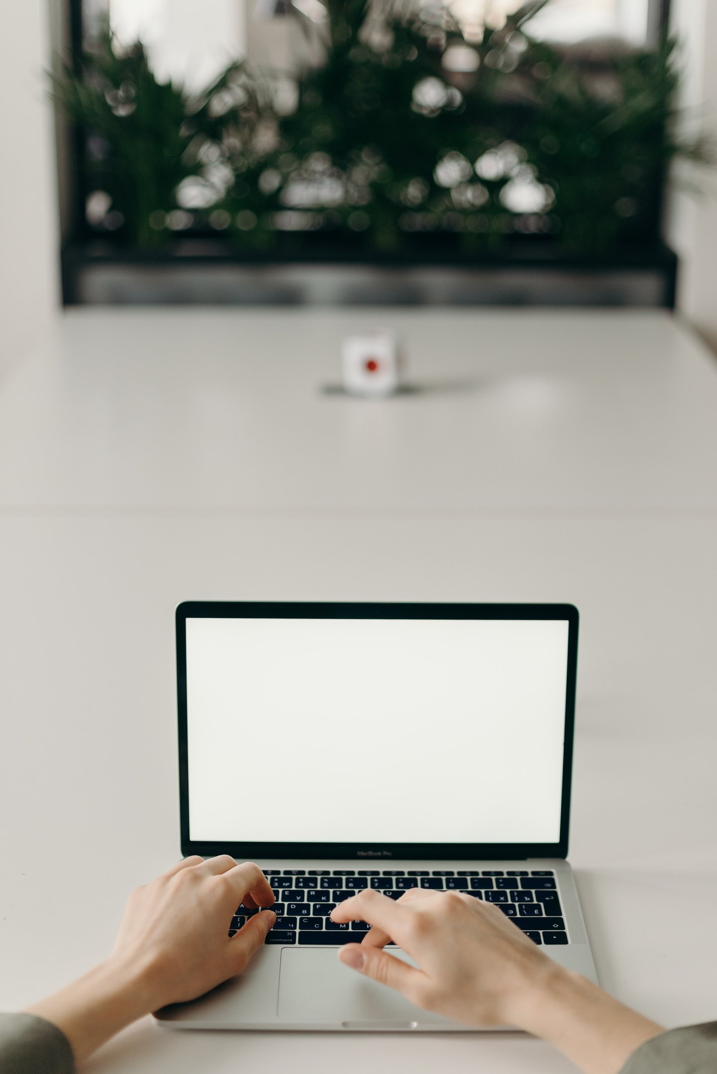 Close-up of two hands using a MacBook which has a white screen. The laptop is placed on a grey platform.