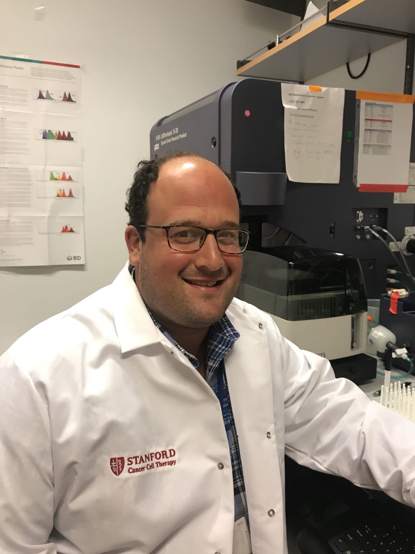 Photo of Dr Robbie Majzner, SAB board member, sat in a lab wearing a white lab coat with the Stansted logo and ‘Cancer Cell Therapy’ written on it.