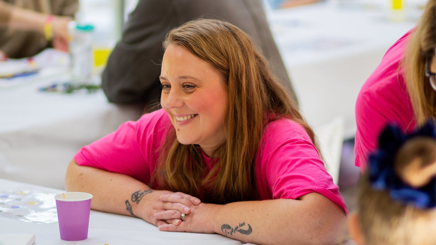 Photo of Solving Kids' Cancer UK Family Support Coordinator wearing a pink charity t-shirt and smiling at a family support event.