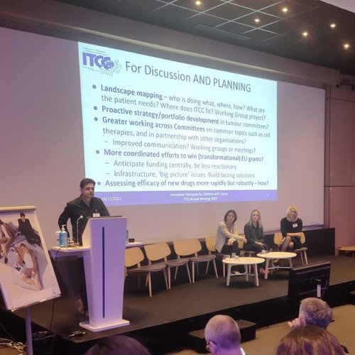 Photo of an SKC member of staff giving a presentation on research advocacy at a conference, with other SKC staff in the background.