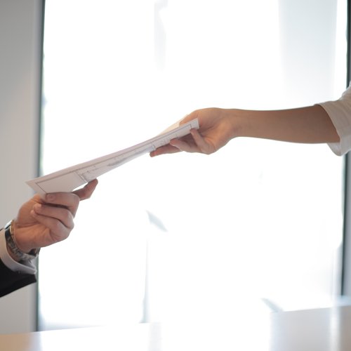 Documents being passed between two outstretched hands.